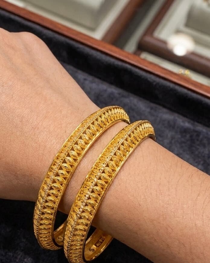 A pair of filigree 22ct gold bangles worn on the wrist, on a velvet tray in the shop
