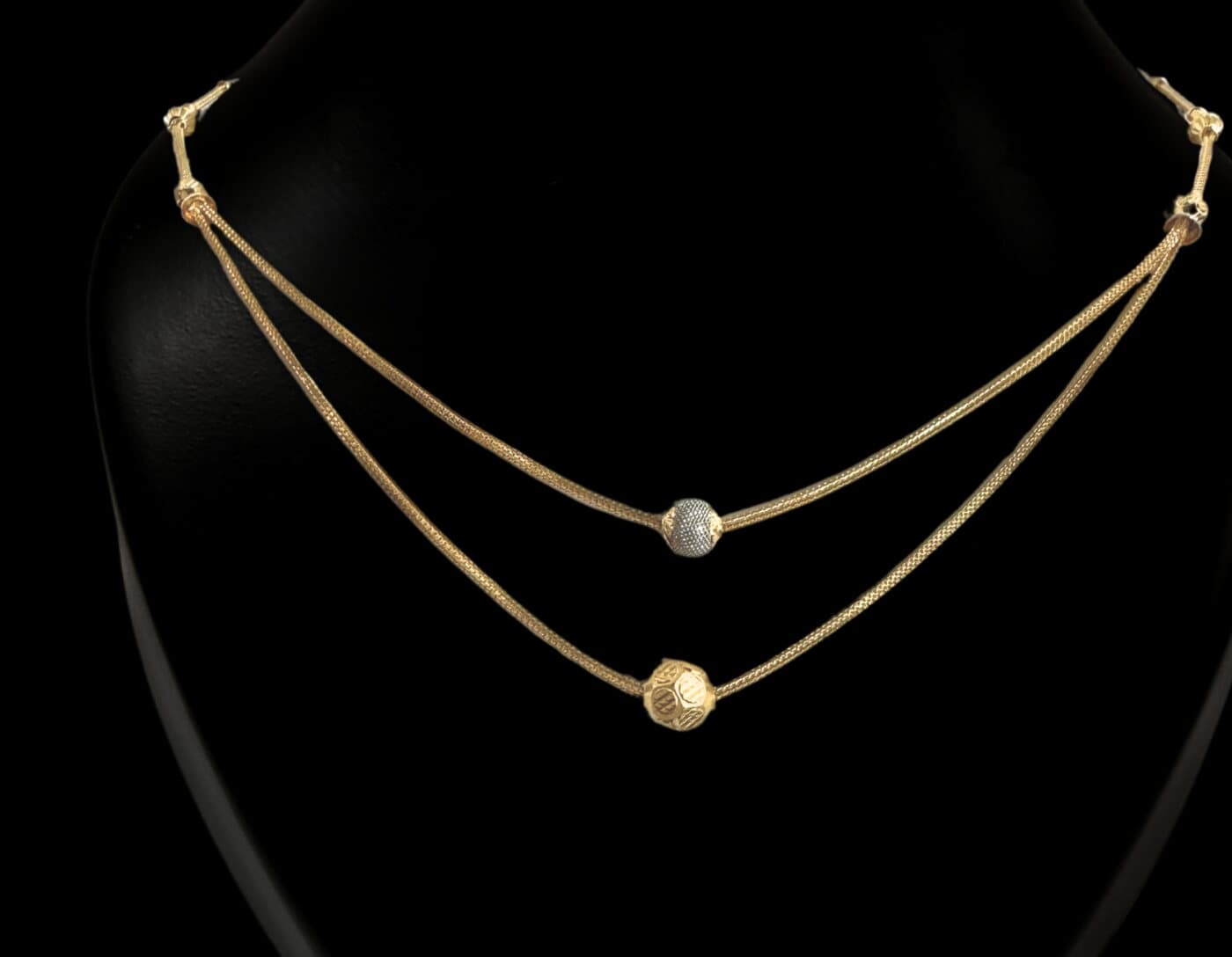A two-strand gold chain with one white and one yellow bead, on a neck stand
