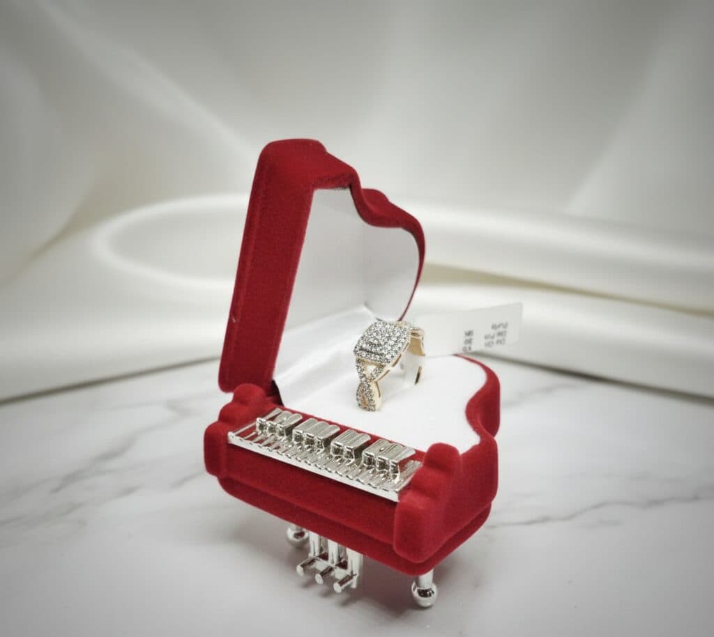 A rose gold ring with a cushion-shaped diamond cluster and a twisted pavé band, in a red piano ring box