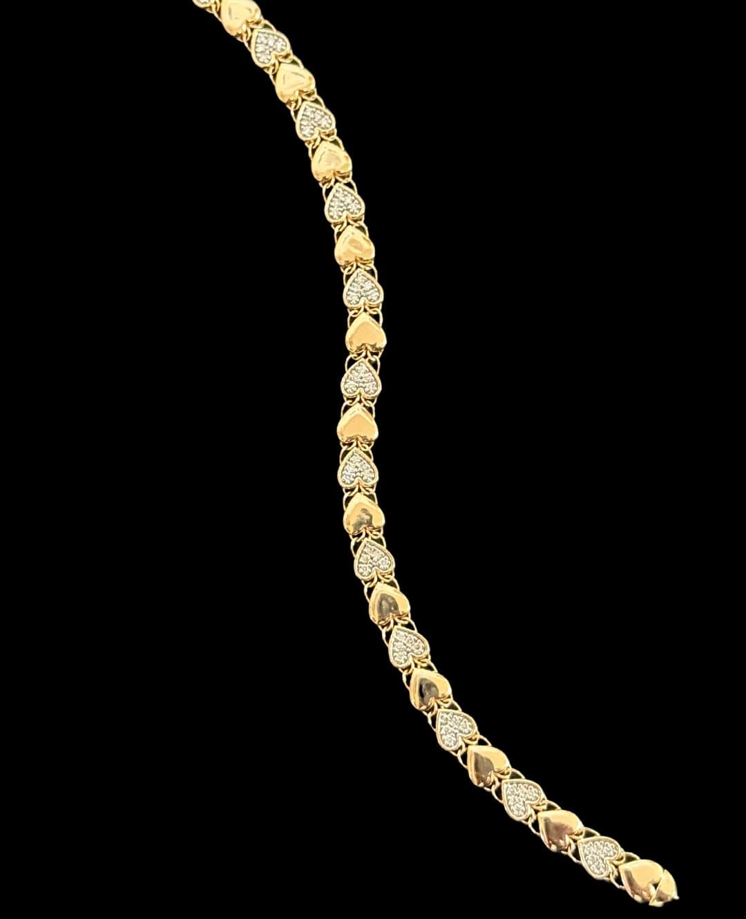 A gold bracelet of alternating polished and stone-set hearts, on black