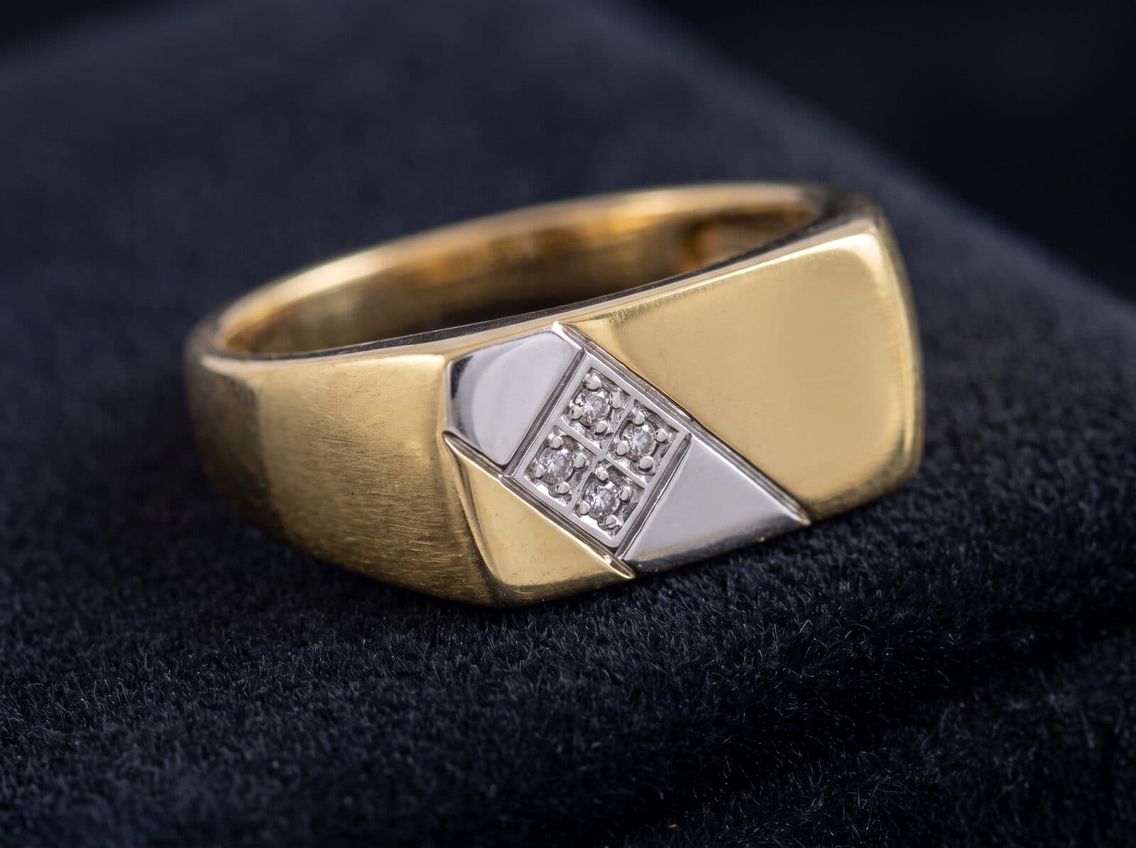 A men's two-tone gold signet ring with a white-gold panel set with small stones, on black velvet